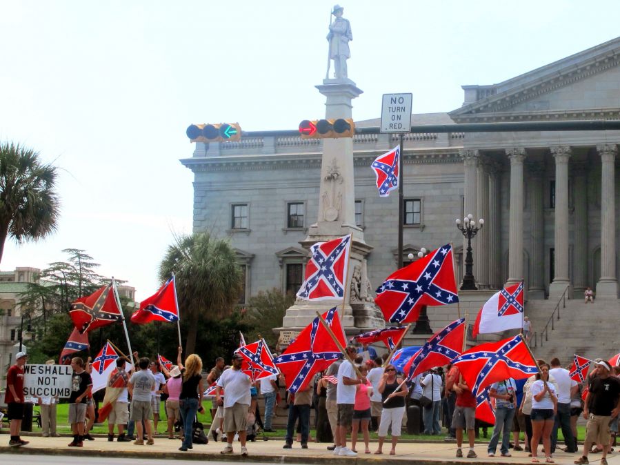 People waving Confederate flags in front of a statue