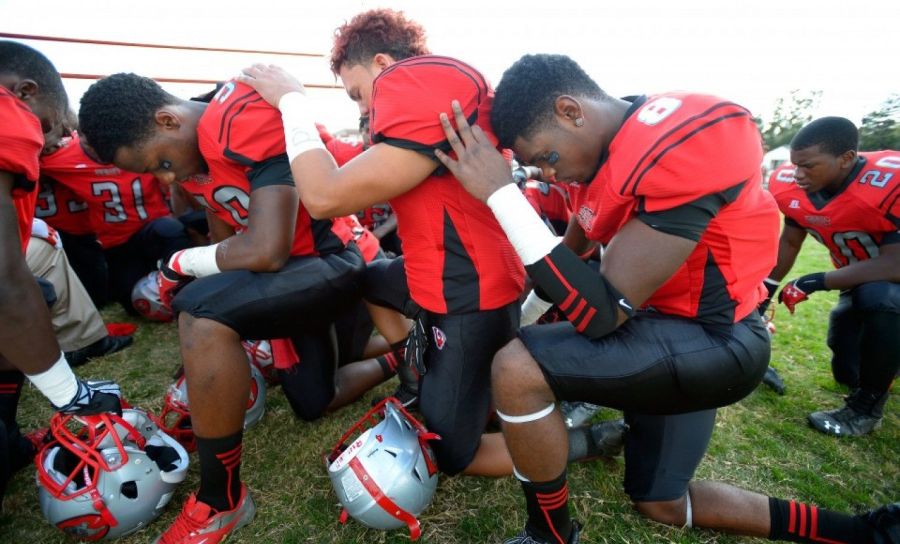 High school football players praying before a game.