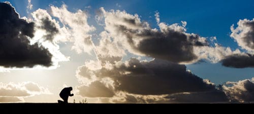 Silhouette of a man praying under cloudy sky