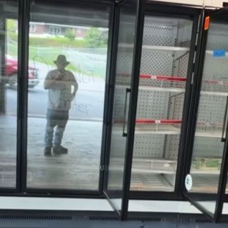 A reflection of Pastor Alvin Christian recording a video in front of empty shelves in his food bank.