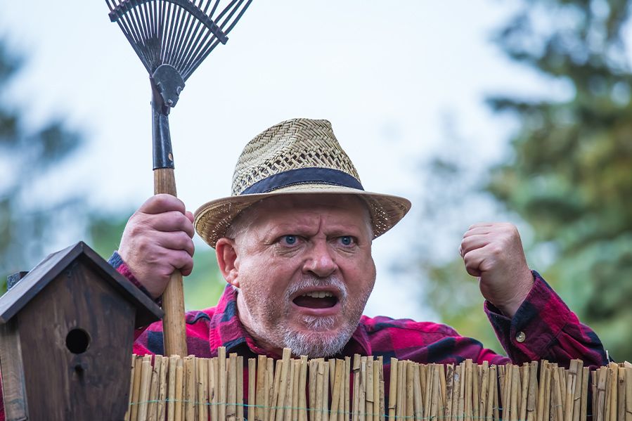angry farmer looking over fence and holding rake