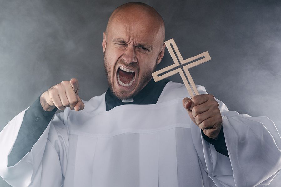 Angry priest holding cross and shouting