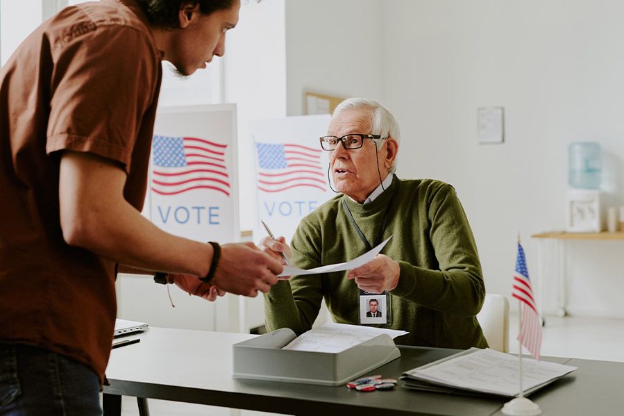 elderly male poll worker helping younger voter