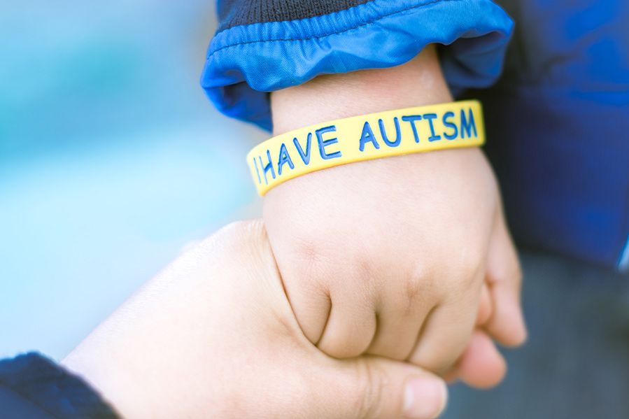 parent holding hand of child with bracelet that says i have autism