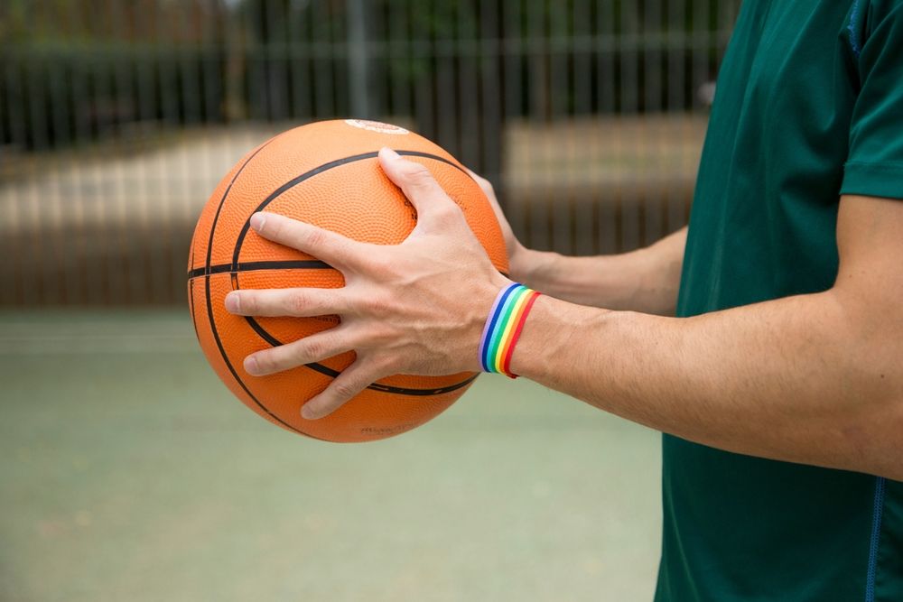A man holding a basketball wearing a pride bracelet