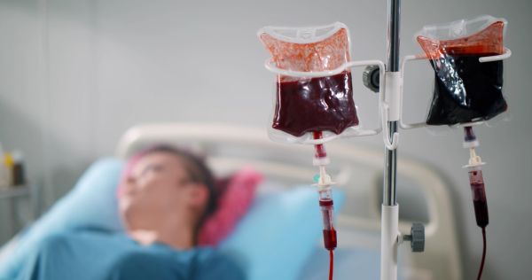 A young patient appears in the background receiving a blood transfusion.