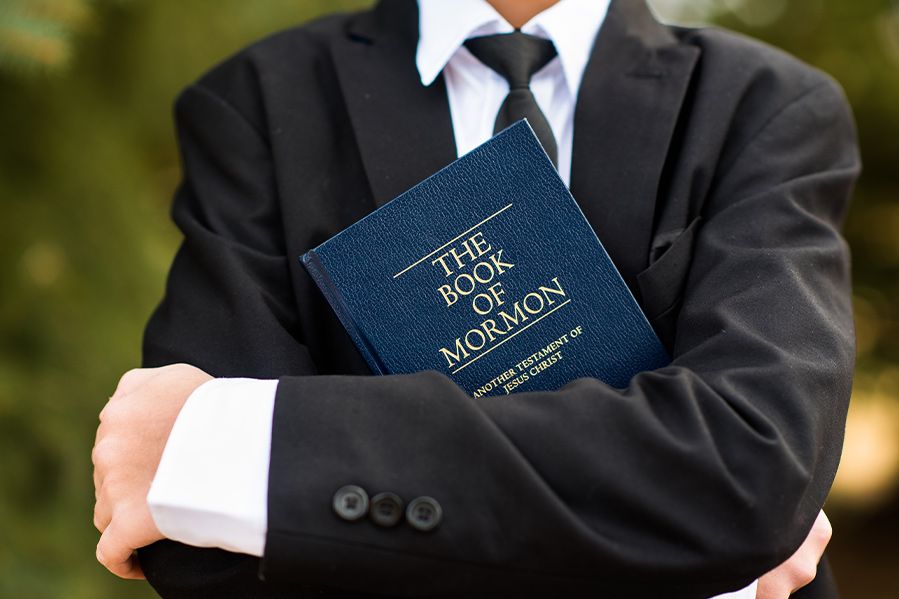 high school student in suit holding book of mormon