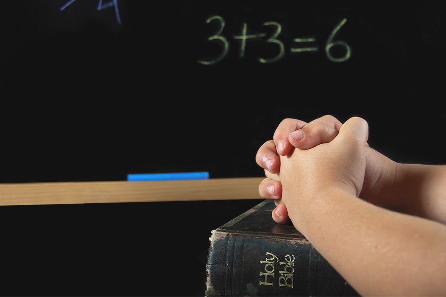 Child's hands folded on Bible in classroom