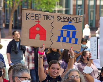 A young woman holds a cardboard sign at a protest advocating that church and state be kept separate.