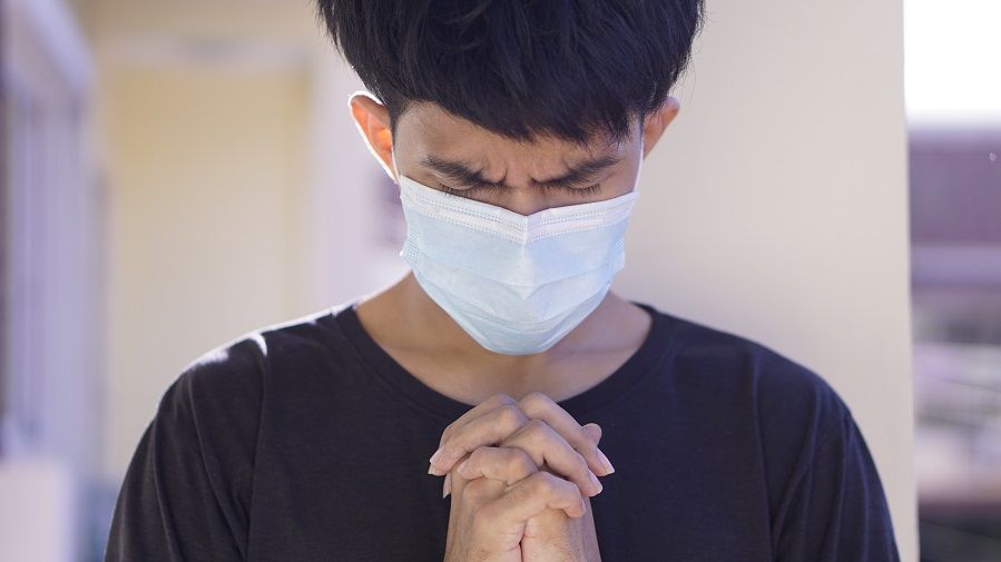 man praying wearing flu mask