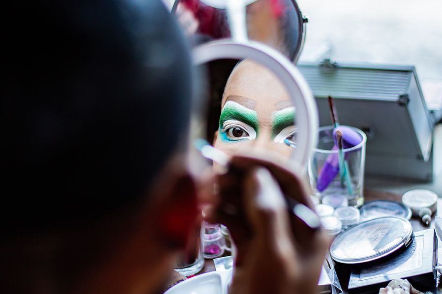 drag queen applying makeup in mirror