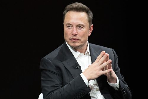 Elon Musk sits stone-faced in a dark room, fingers tented ominously.