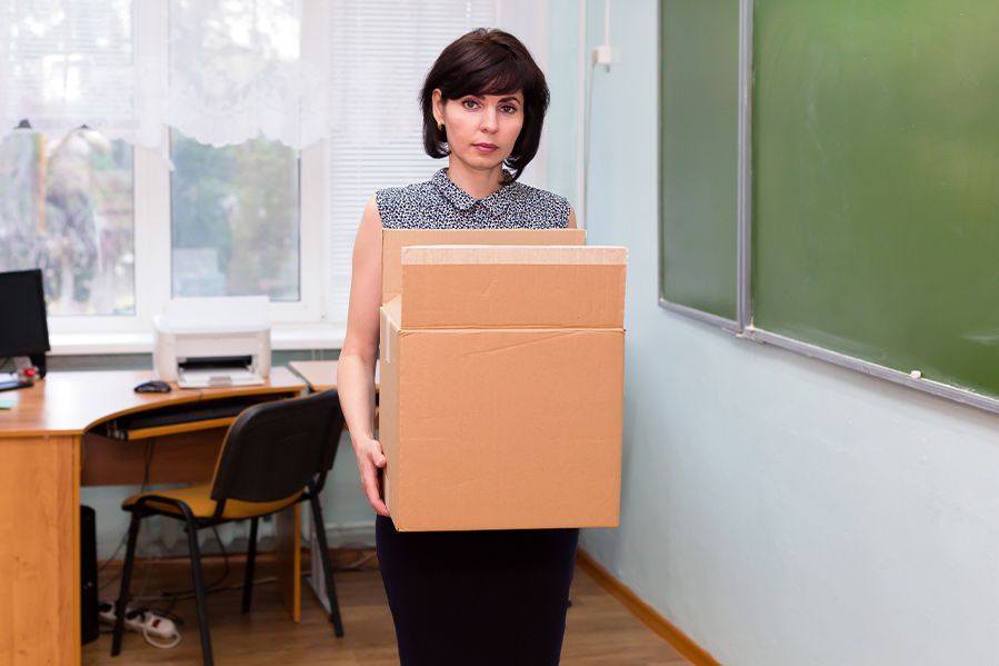 fired teacher holding cardboard box in classroom