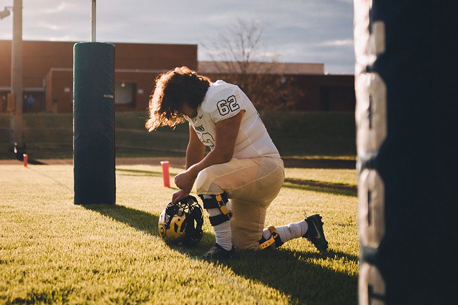 football player kneeling in prayer on field