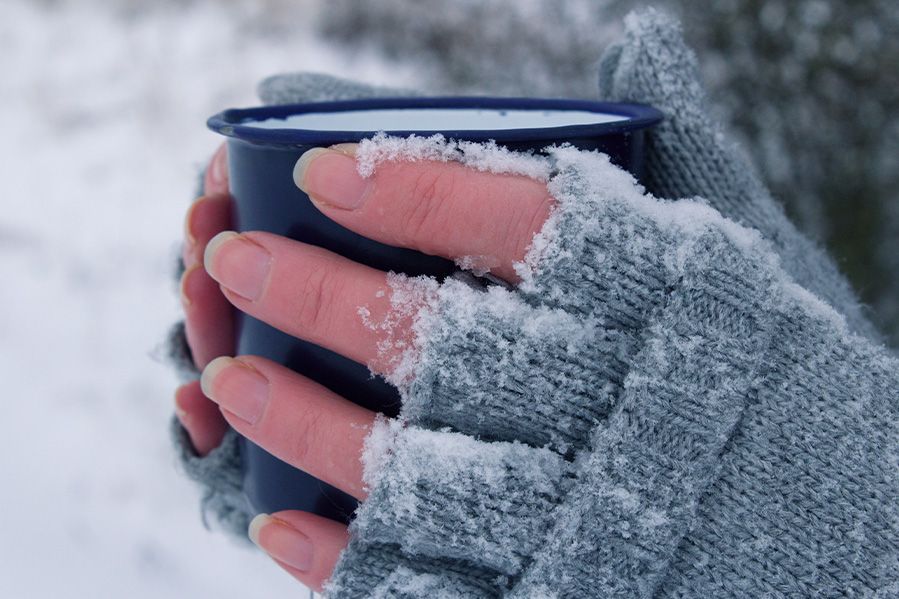 frozen hands of homeless woman holding mug of coffee in the cold
