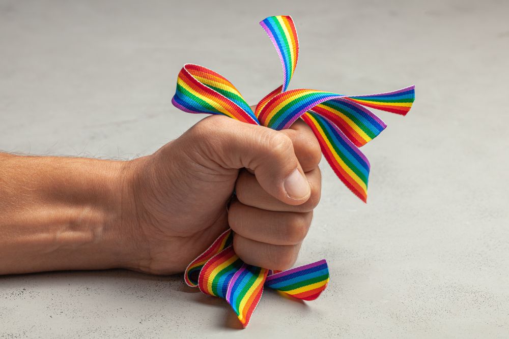 A man's hand angrily clutching rainbow gay pride ribbons