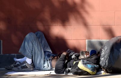 A homeless man sleeps beside a building