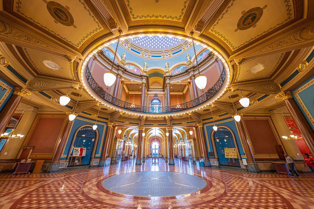 The interior of the ornate rotunda of the Iowa state capitol building, with gold, red, and blue stonework throughout,