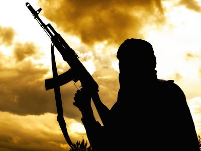 A person in traditional Islamic robes holds an assault-rifle style gun pointed into the air.