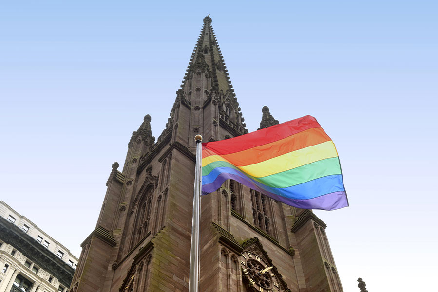 An lgbt pride flag flying in front of a church