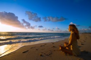woman meditating on beach at sunset