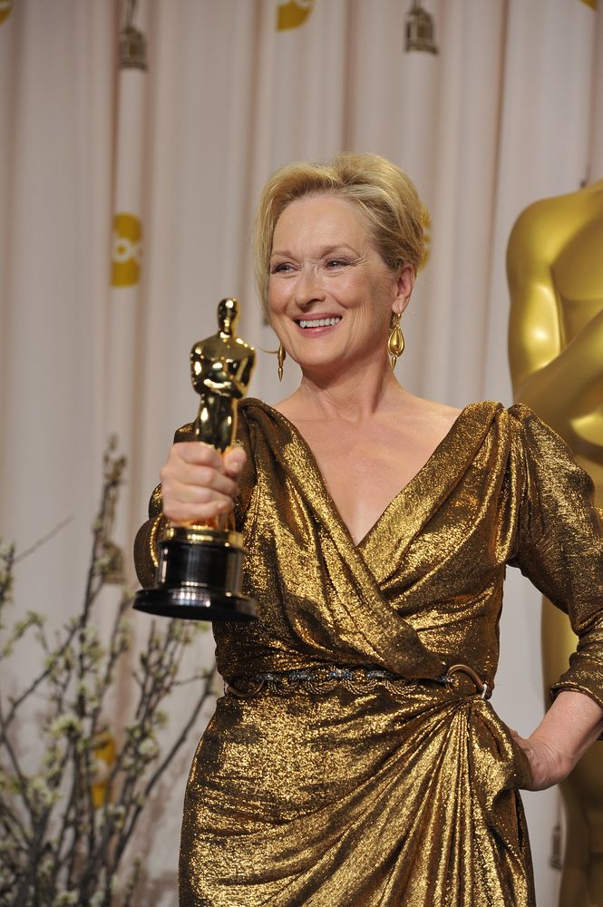 Actor Meryl Streep in a gold dress proudly displaying an Academy Award