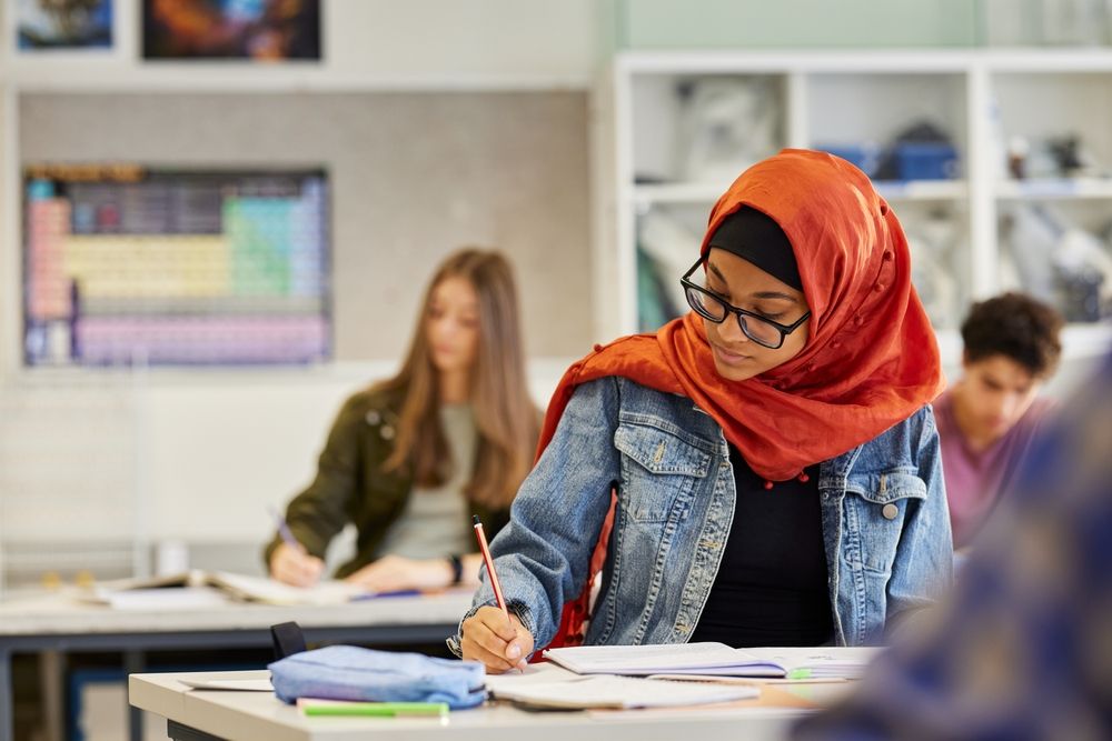Student wearing a hijab writes in a notebook during class.