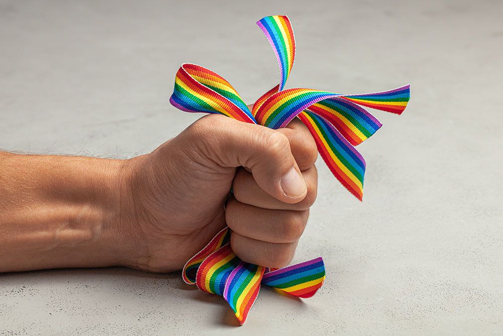 A male hand angrily clutches rainbow pride ribbons