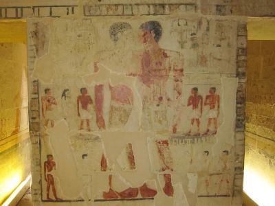 An illuminated section of a tomb depicts fading paintings of two men apparently touching noses to one another.