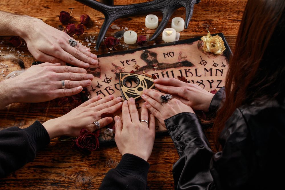 Hands resting on a Ouija board during a seance, surrounded by candles.