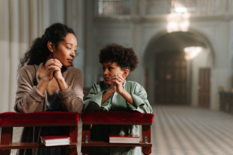 Parent and child praying together inside a church.