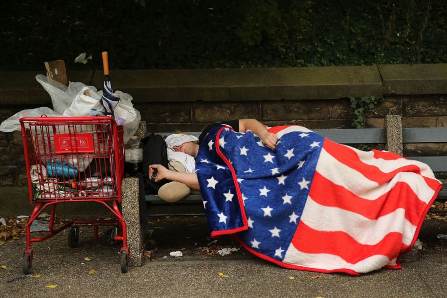 homeless man laying on street draped in American flag