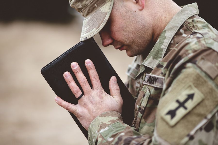 US servicemember in uniform praying with Bible