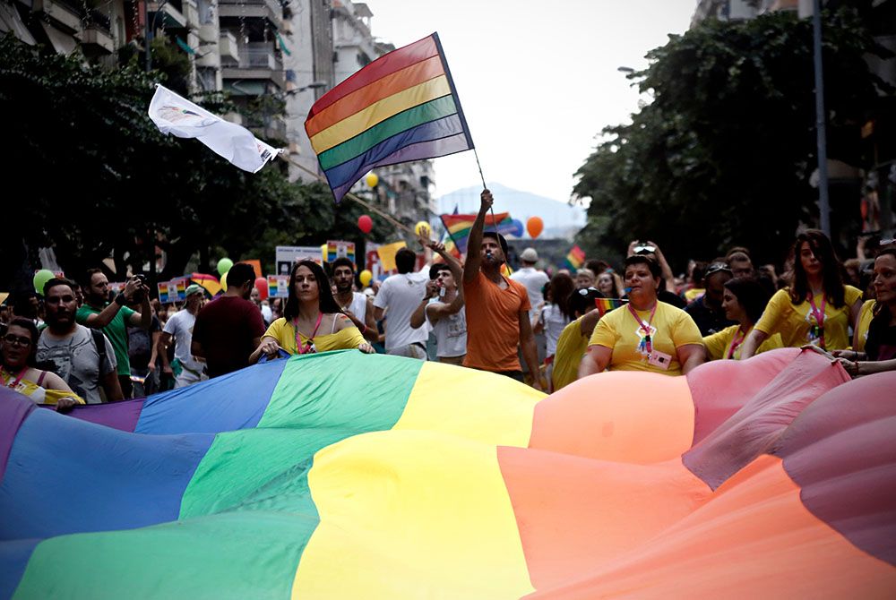 A group of people marching at a pride parade carrying a large pride flag and displaying another.