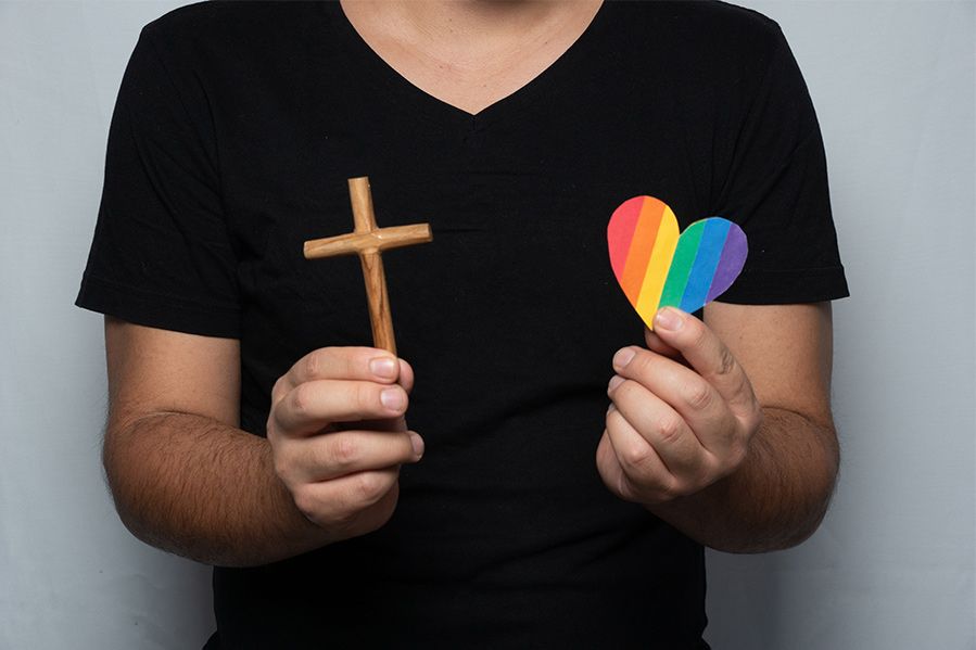 man holding rainbow heart and christian cross