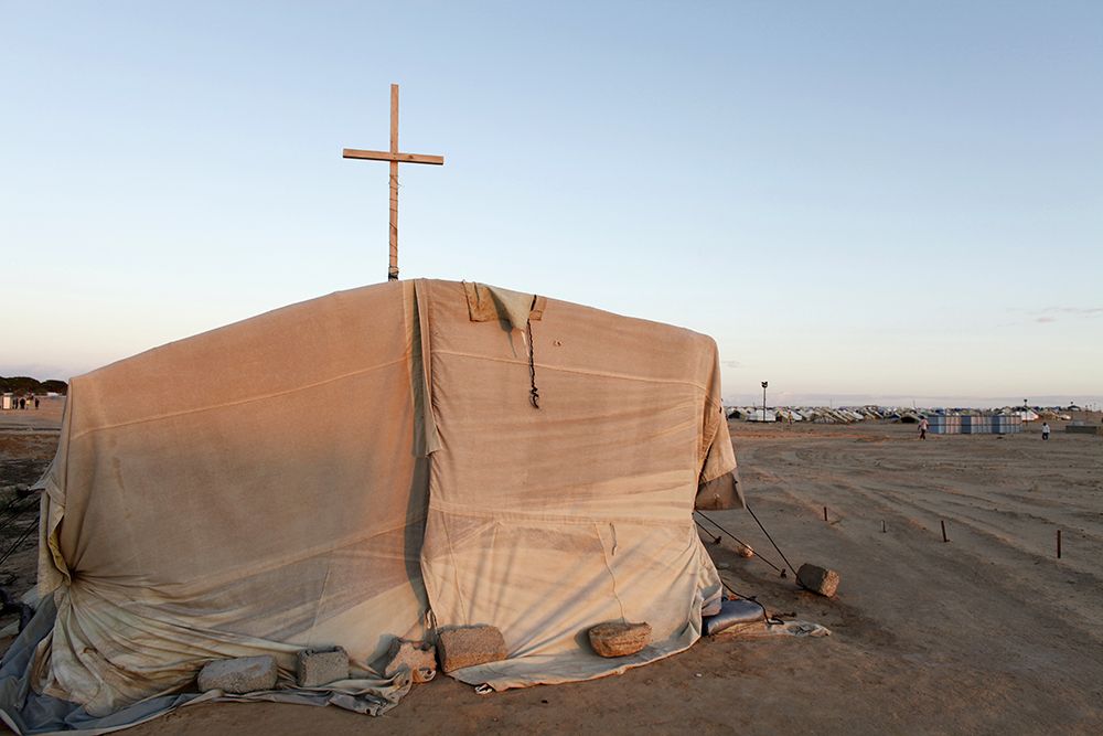 A makeshift tent church with a narrow wooden cross in a refugee camp.