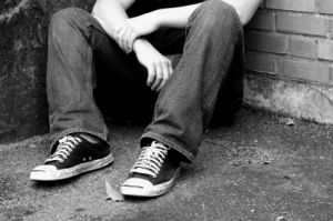 youth sitting on pavement against brick wall