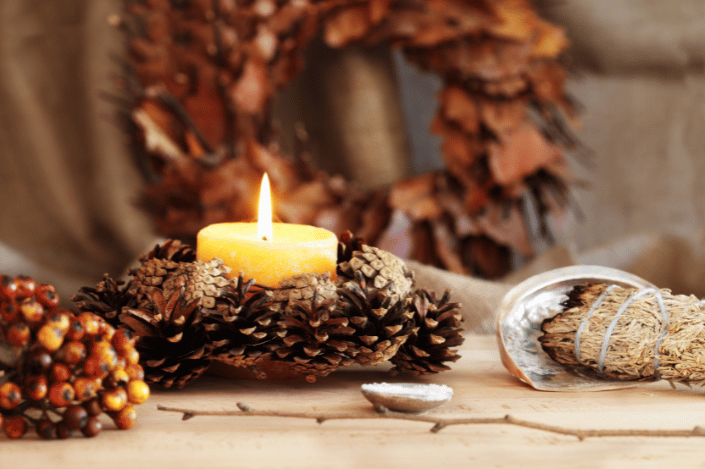 Lit candle surrounded by pinecones, autumn decor, and bundled herbs for a Samhain celebration.