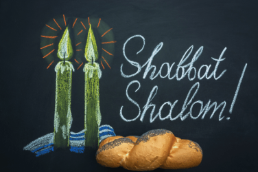 Shabbat candles and challah bread beside a chalkboard reading Shabbat Shalom