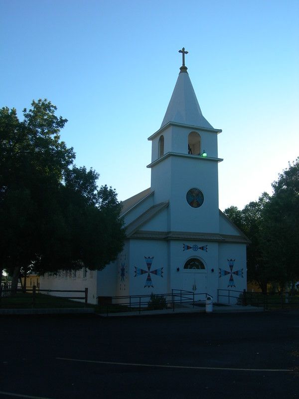 White St. Stephens Mission Church decorated with Arapaho-inspired geometric designs beneath a blue Wyoming sky.