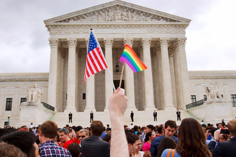 person waving pride flag and american flag in front of supreme court