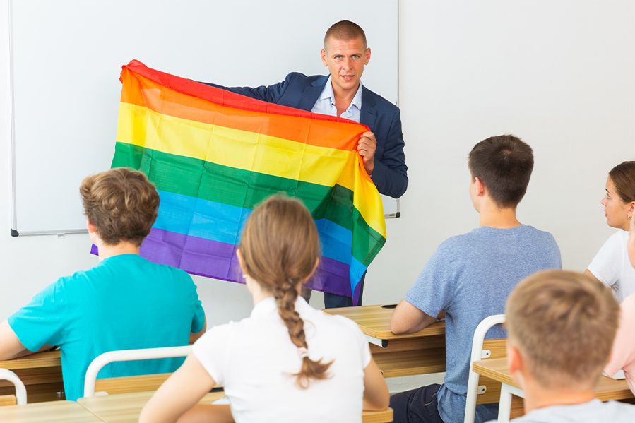 male teacher holding rainbow gay pride flag in front of class