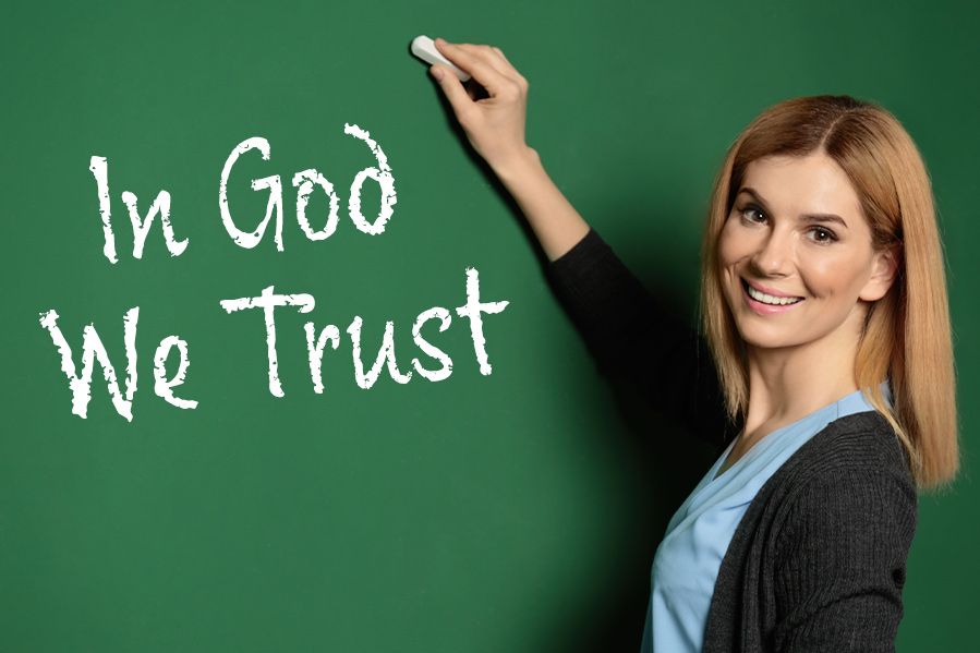 teacher writing in god we trust on blackboard