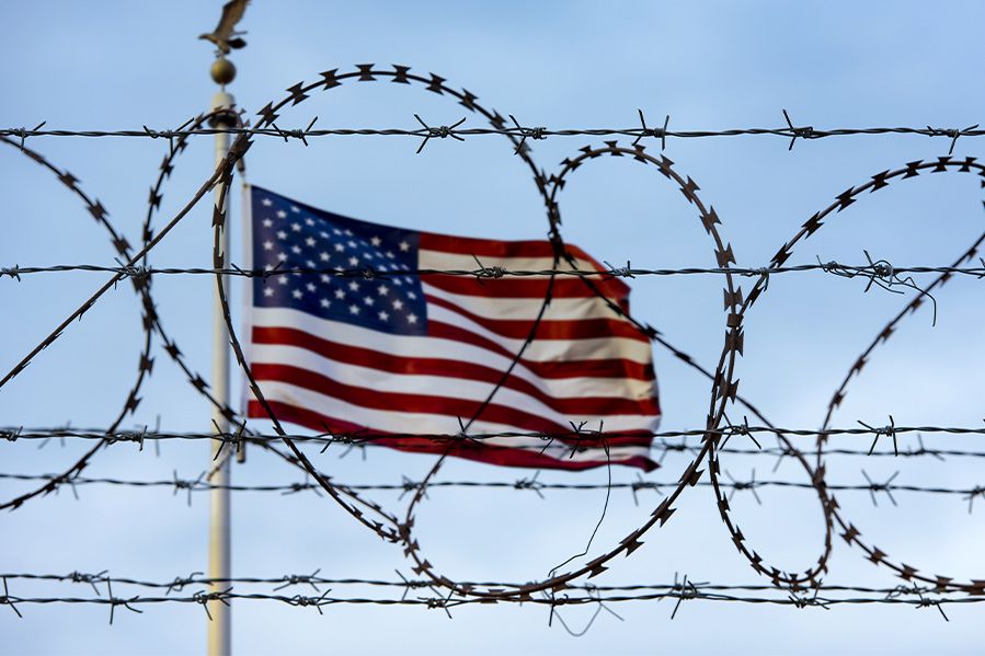 united states flag behind barbed wire at mexico border
