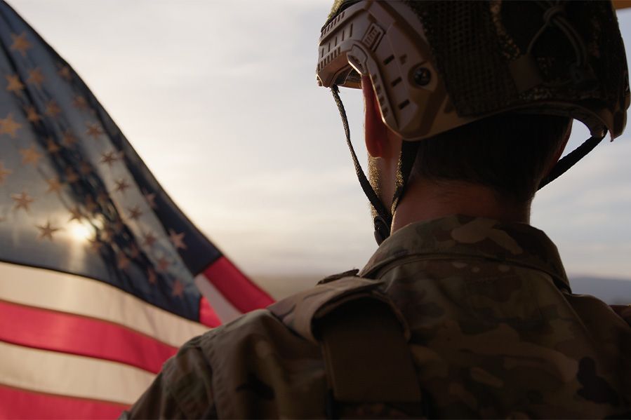 man in military fatigues looking at united states flag in distance