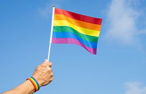hand holding mini pride flag in front of bright blue sky
