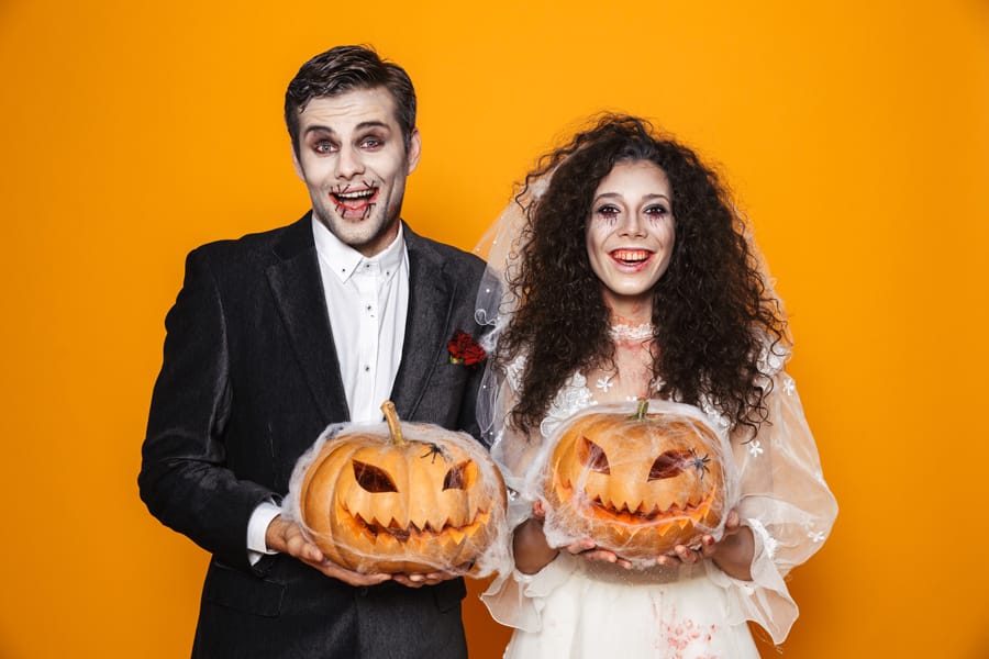 Bride and groom in zombie makeup holding jack-o-lanterns at Halloween wedding