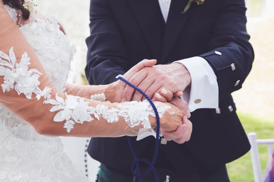Groom tying handfasting cord around bride's wrist at wedding