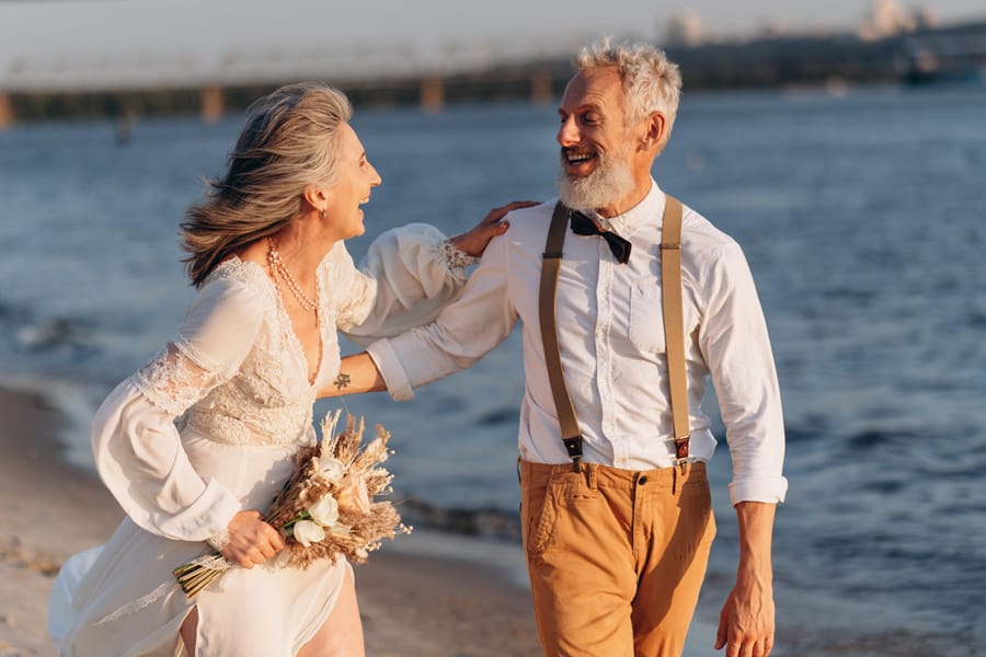Elderly newlywed couple in love walking down beach