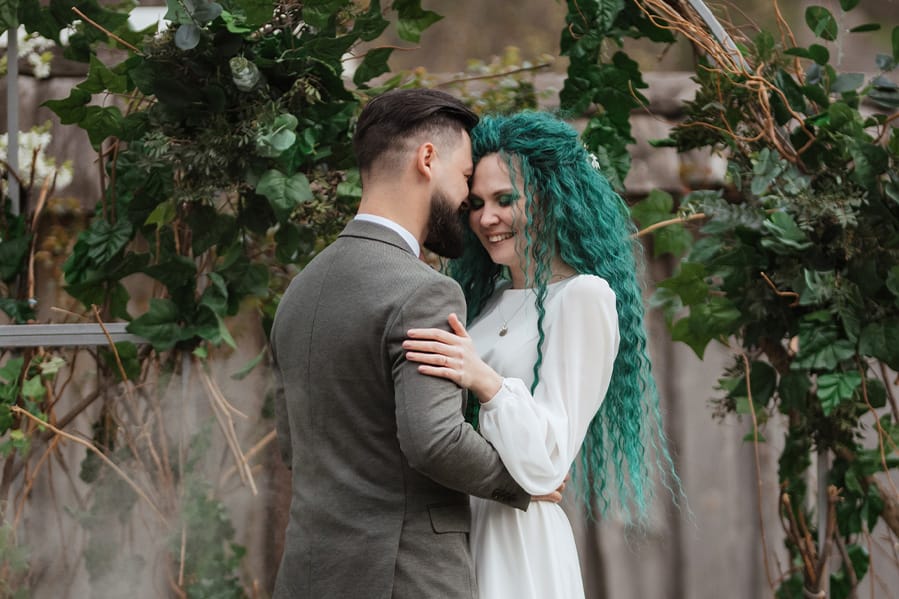 A couple being married outside with some greenery at the altar.